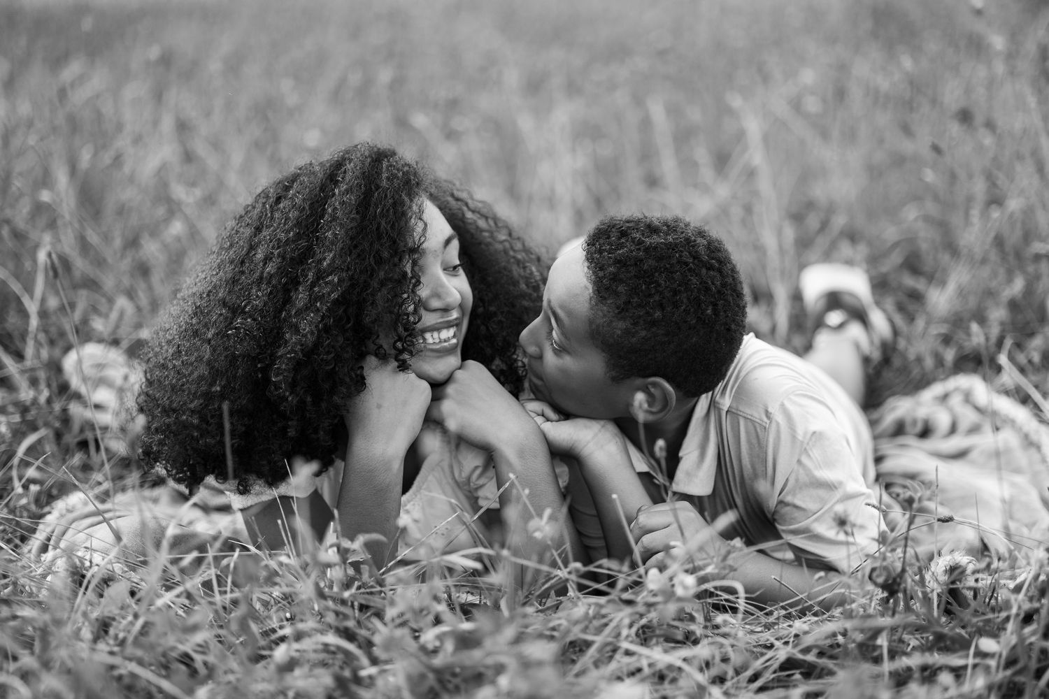 A couple lying in grass field sharing an intimate black and white candid moment together.