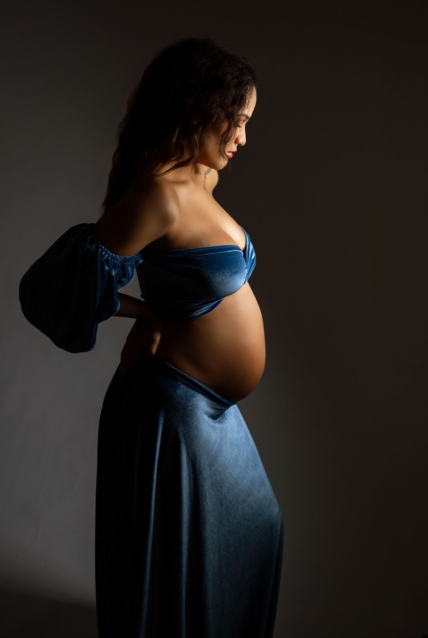 A series of silhouetted maternity photos showing a pregnant figure in a blue dress against a dark background.