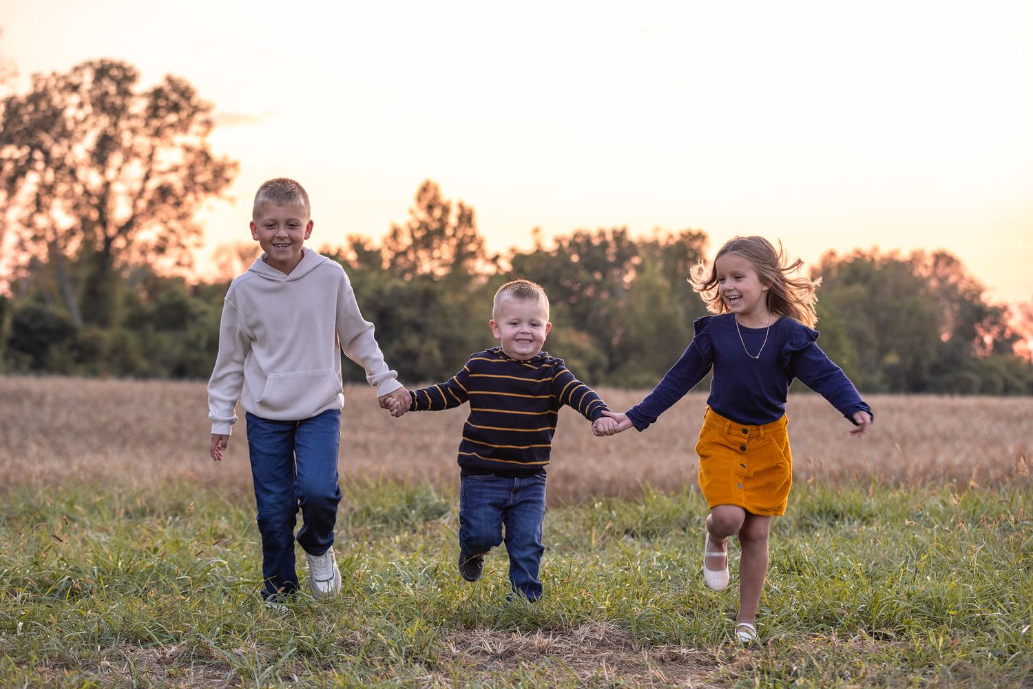Three children running and playing together in a field at sunset.