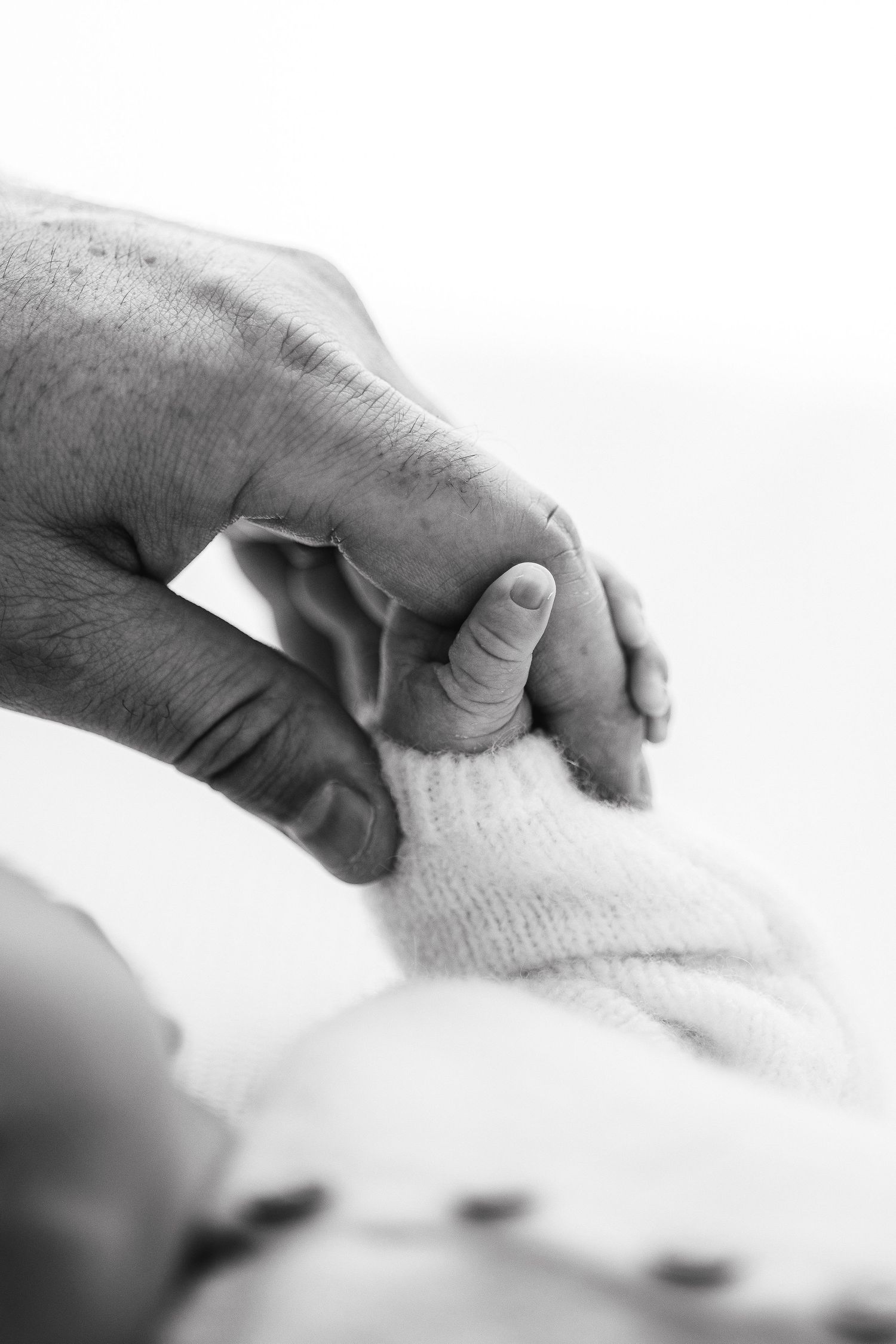 Black and white close-up image of adult hand holding tiny infant sock with tender care.