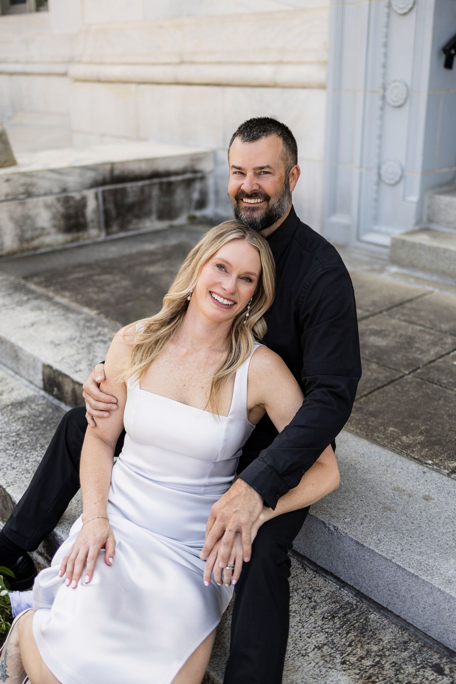 A couple in contrasting black and white outfits sitting together on stone steps and sharing a happy moment.