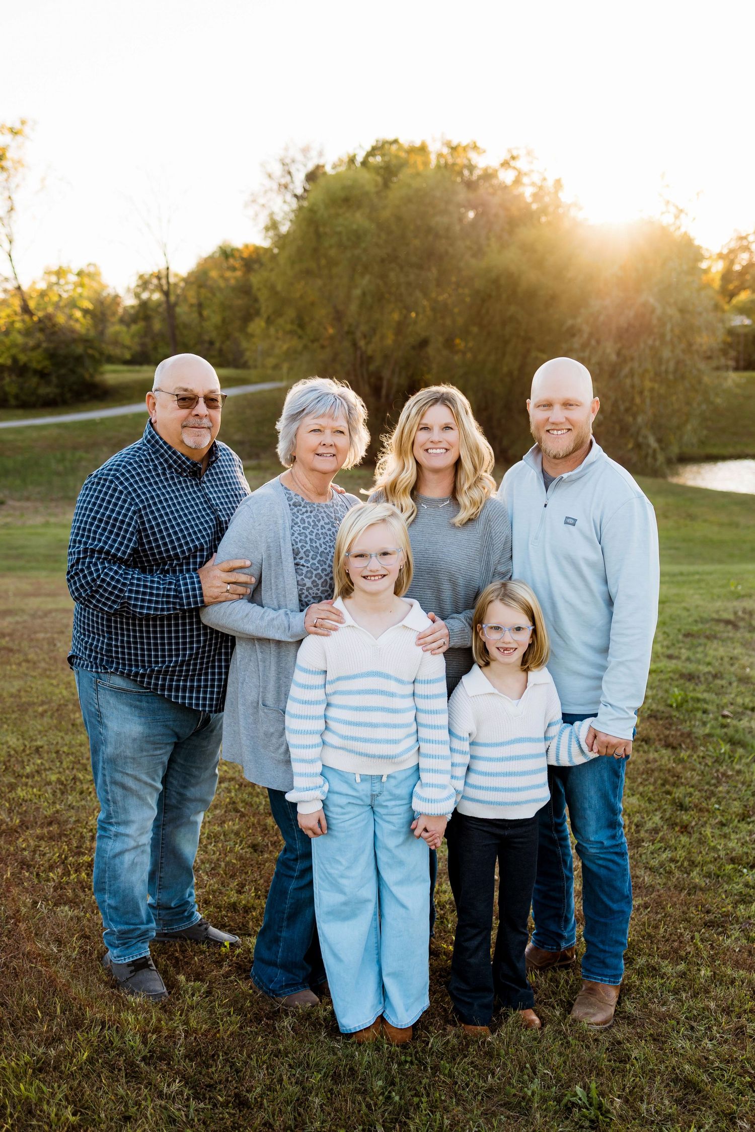 A family group poses together in a grassy field at golden hour with sunlight glowing behind them.
