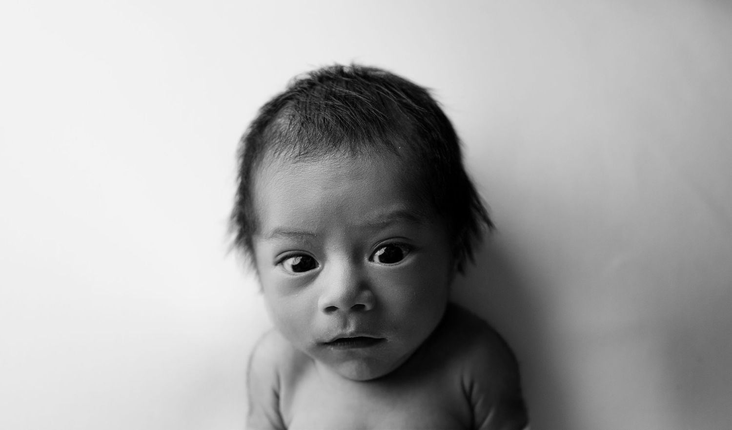 A black and white photo shows a baby's face in close-up view with soft lighting and gentle shadows.