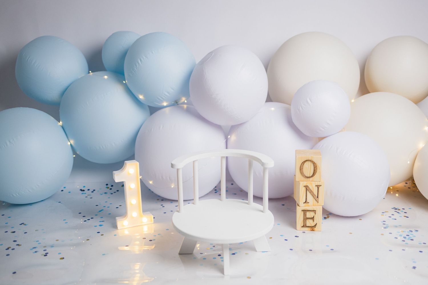 Illuminated number one candle with blue and white balloons and party decorations for first birthday celebration setup.