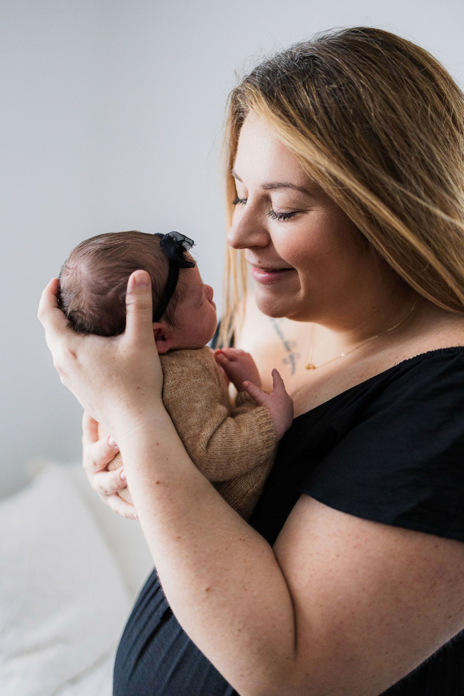A tender moment captured between parent and newborn baby in black clothing against a light background.