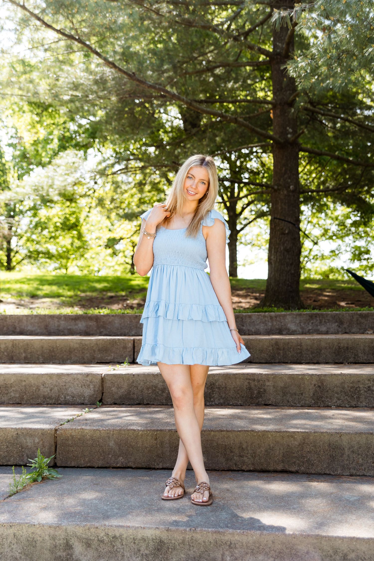 Series of shots showing someone in a light blue ruffled dress sitting on concrete steps in a sunny outdoor setting.