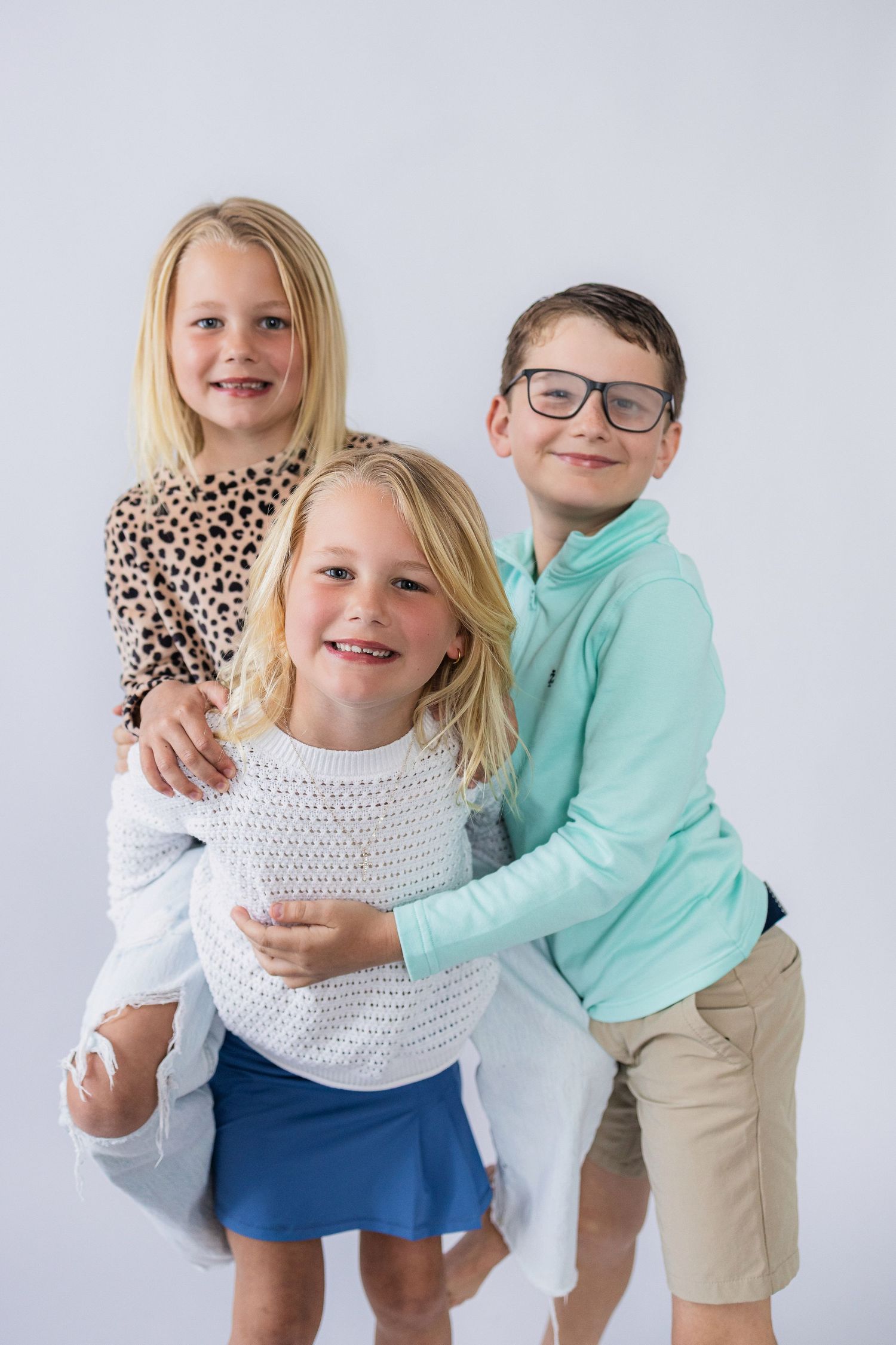 Children in casual attire pose together, wearing a leopard print top, white sweater, and mint green shirt.