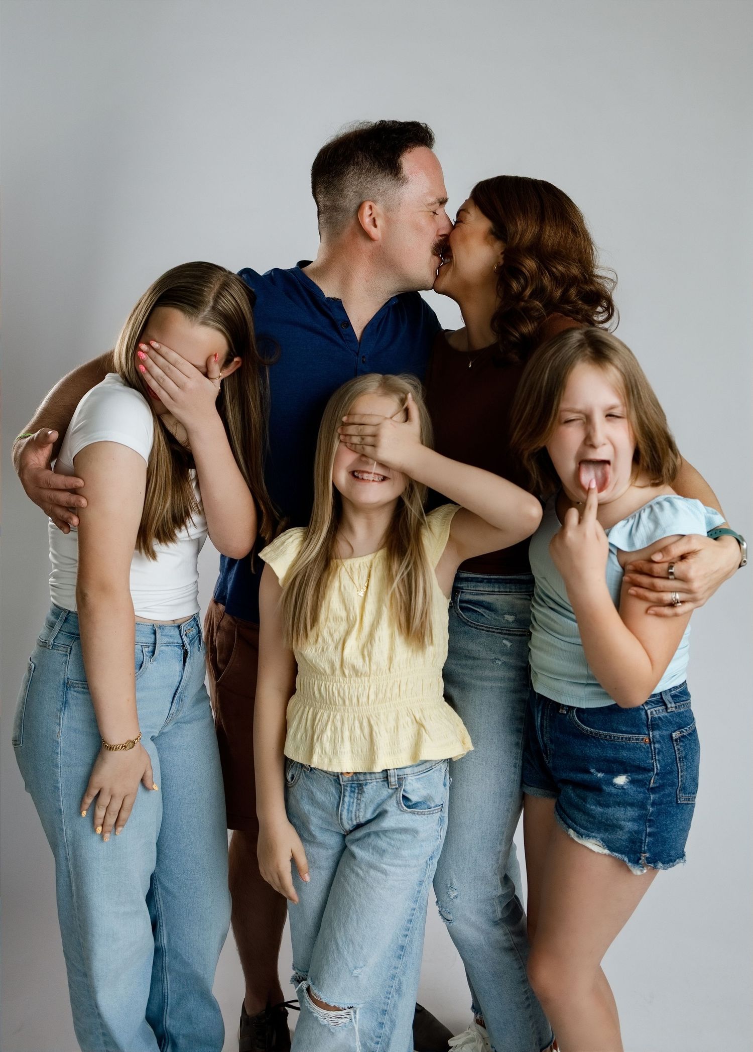 Parents kissing while their three daughters make playful faces during an Edwardsville studio family session