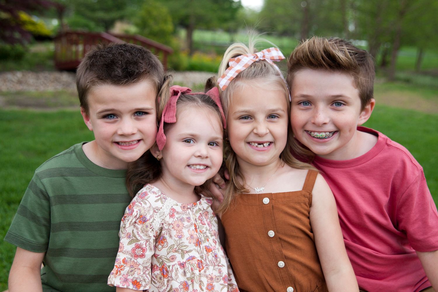 Group photo of four children smiling together outdoors in casual attire.