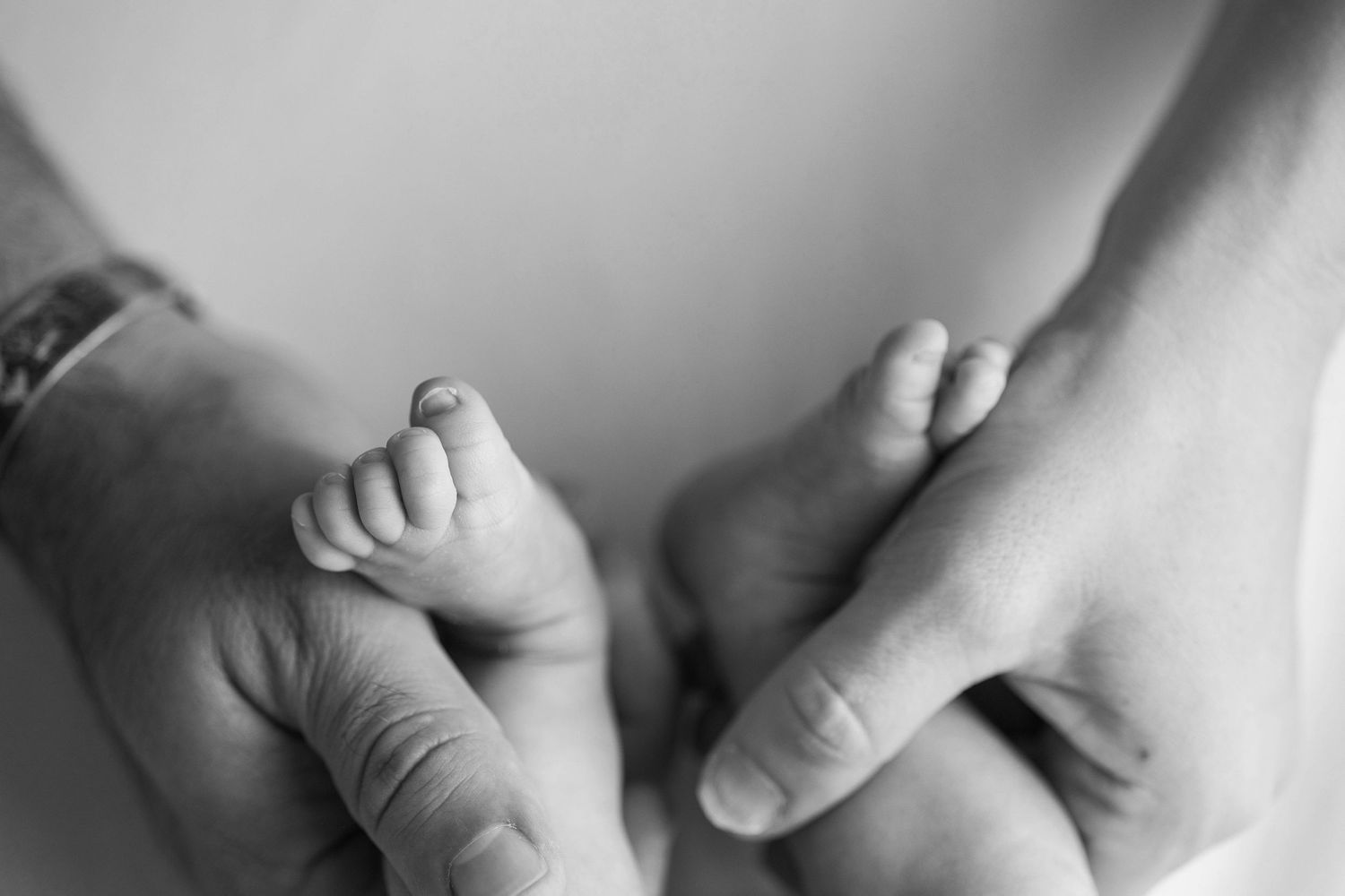 Close-up black and white photo of tiny newborn baby feet being gently held by adult hands.