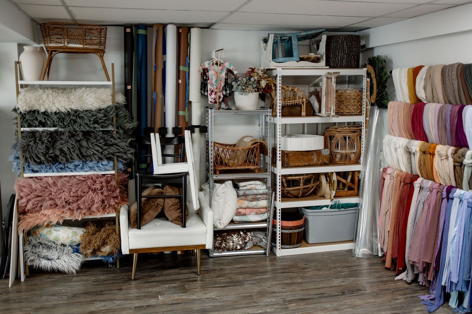 A vintage photography studio interior with backdrops, props, and fabric drapes arranged along white walls.