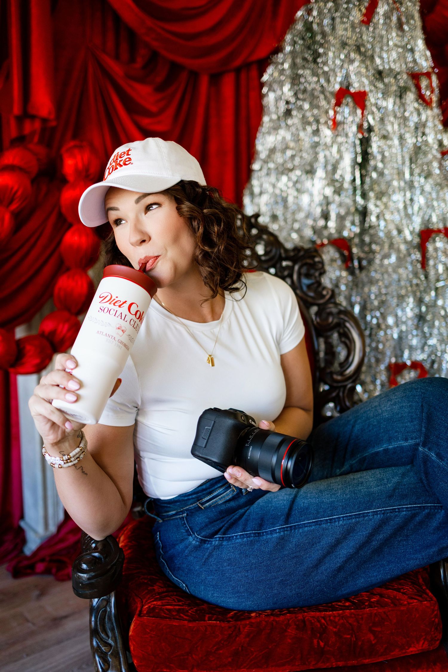 Photographer relaxes on red couch with drink against sparkly silver backdrop.