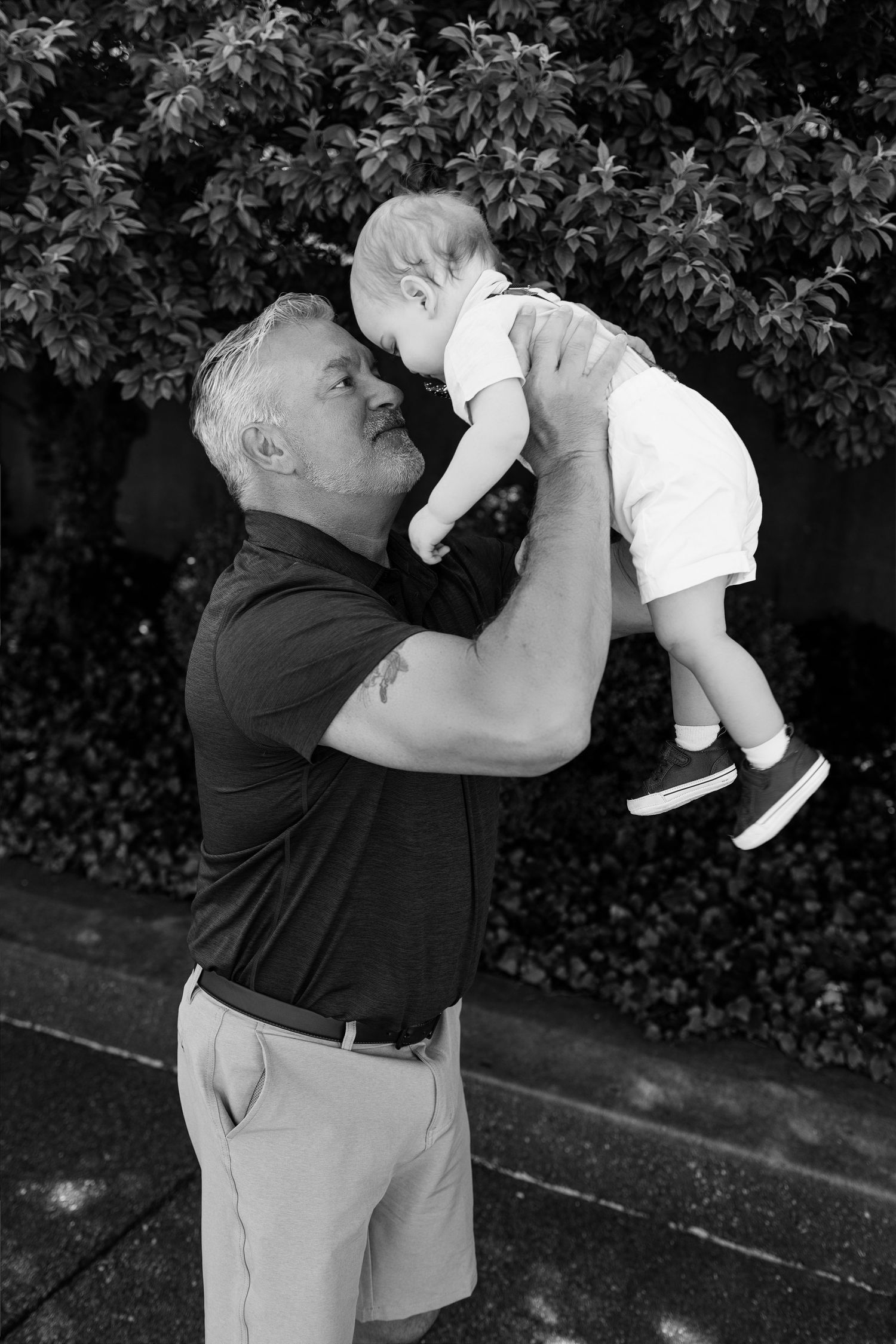 Black-and-white portrait of a man lifting a baby during a playful family photography session