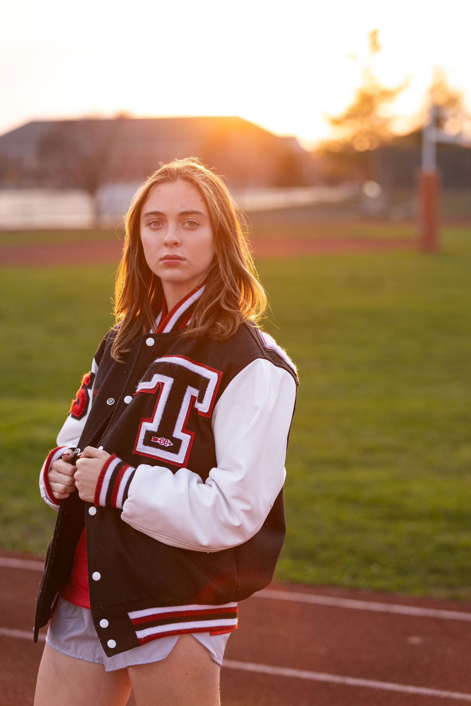 Athletic portrait featuring varsity letterman jacket at sunset on running track.