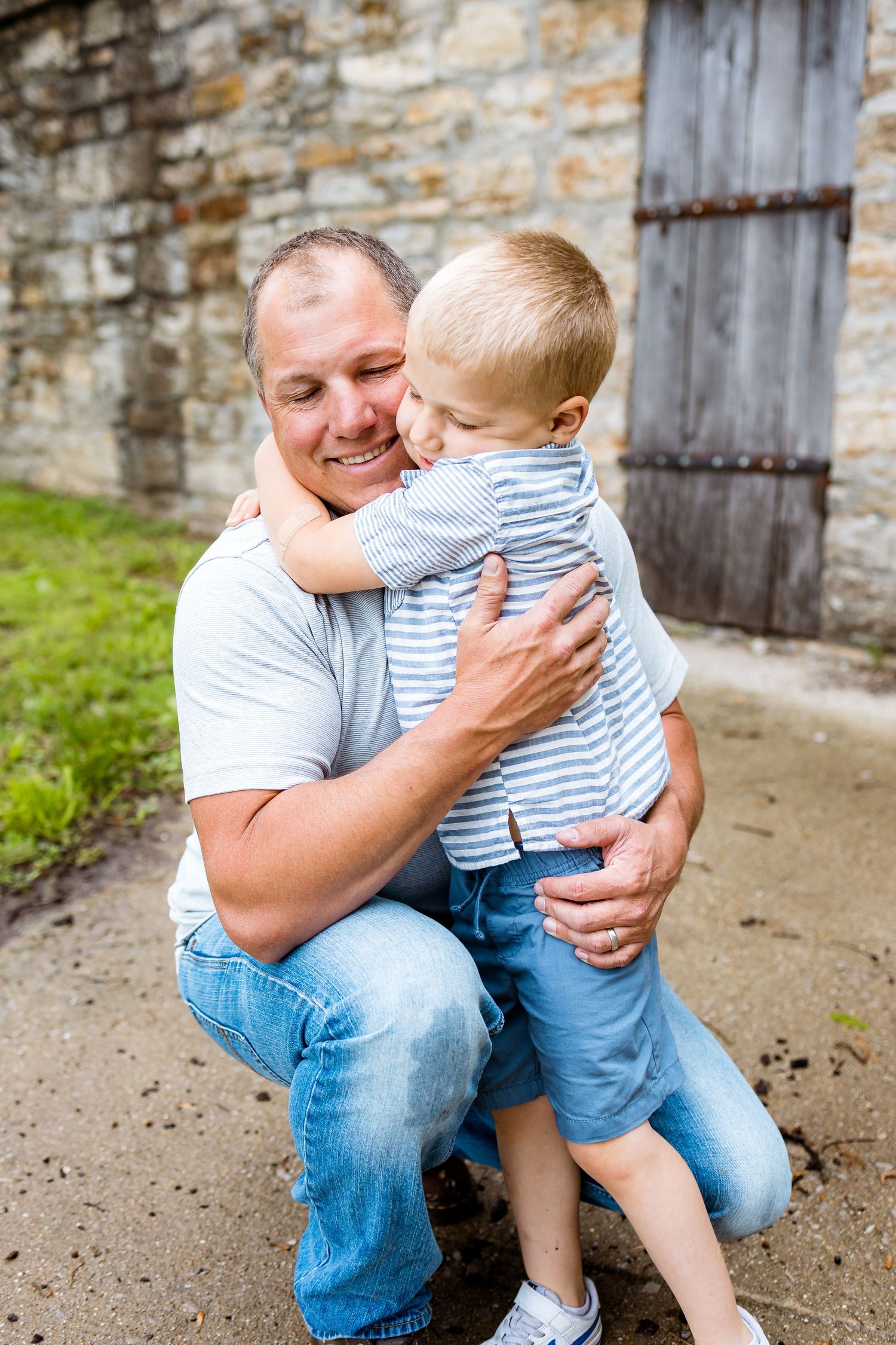 Father and son sharing joyful embrace by rustic stone wall.