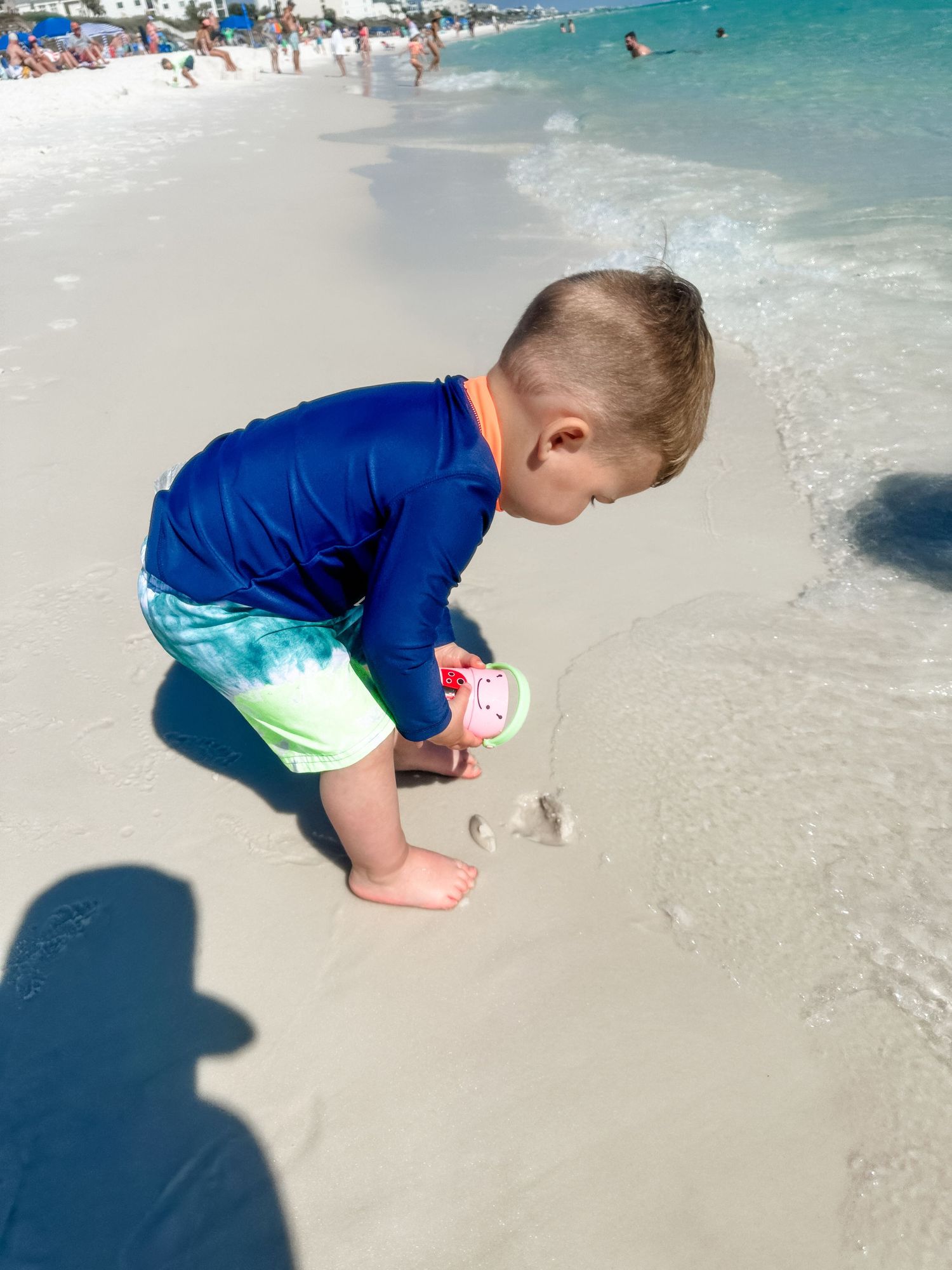 Young beachgoer in blue swimwear explores the wet sand at the water's edge.