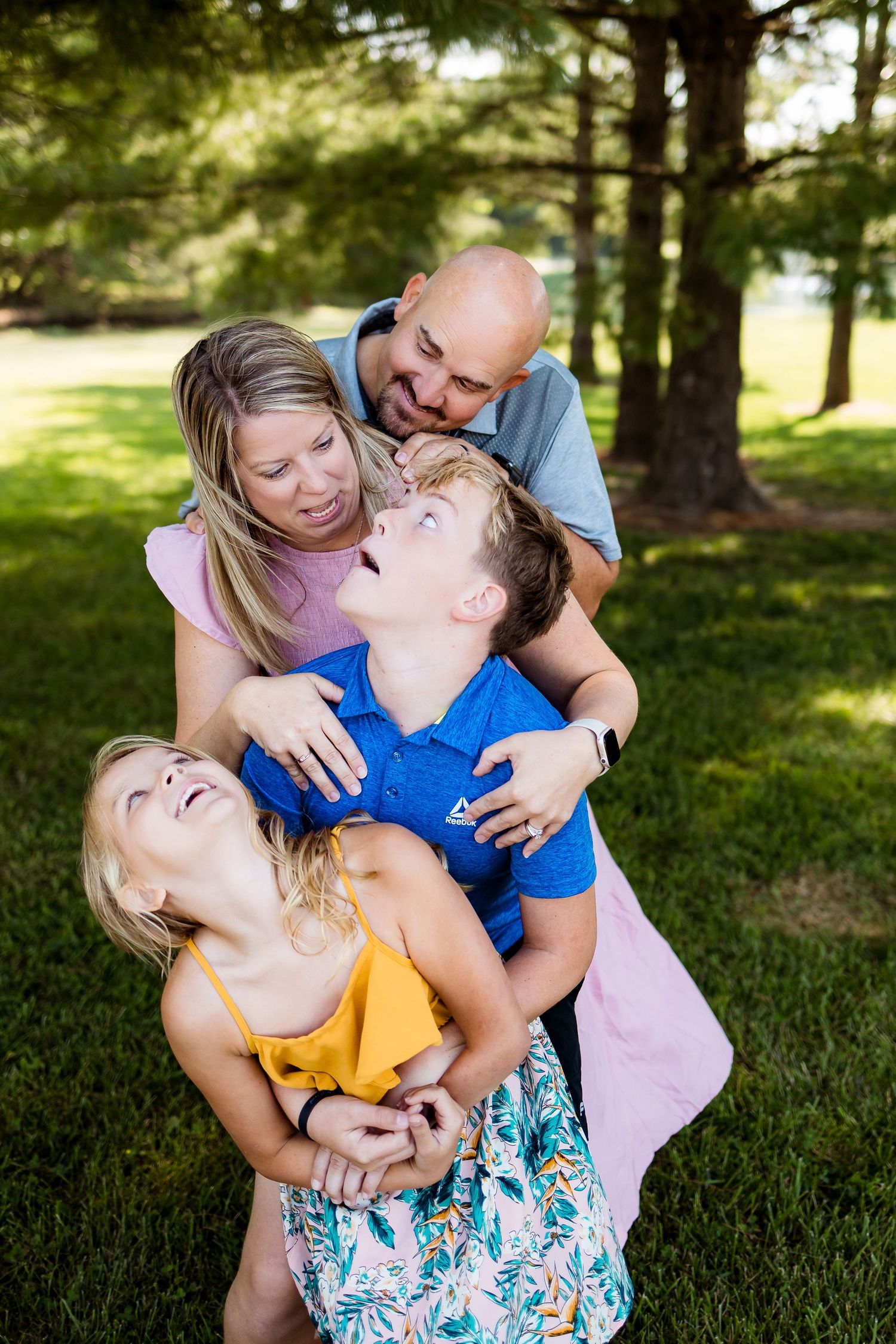 A joyful family moment captured outdoors with bright smiles and hugs in a natural setting among pine trees.