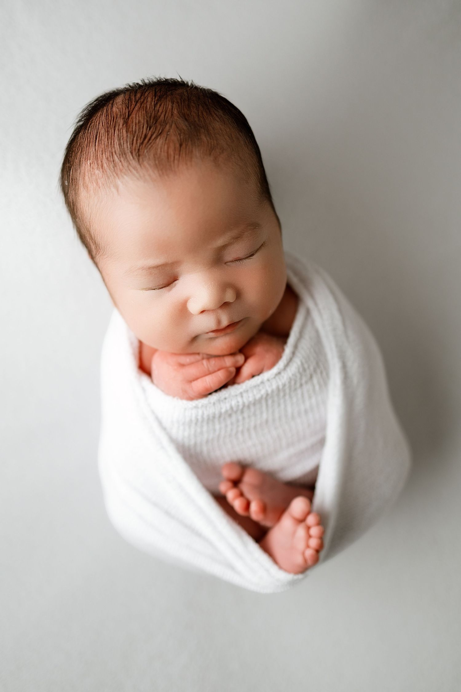 A sleeping newborn baby wrapped in white fabric shown from multiple angles in a minimalist photography series.