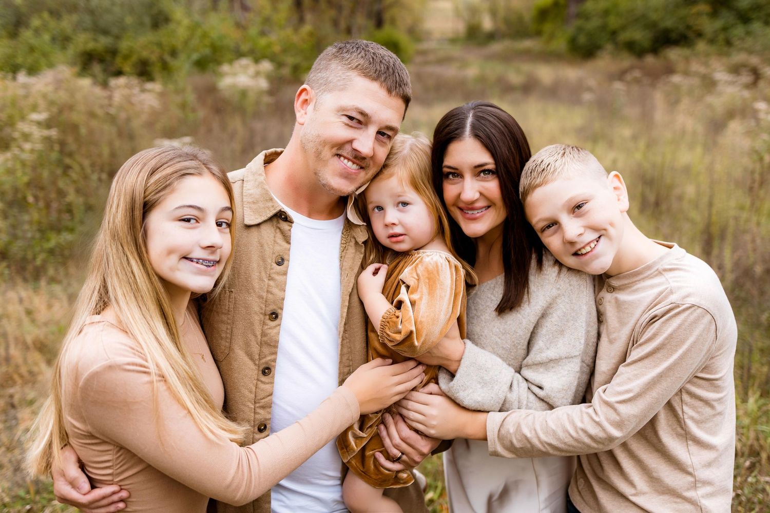 A group of people in coordinated neutral-toned outfits pose together outdoors in a natural setting during golden hour.
