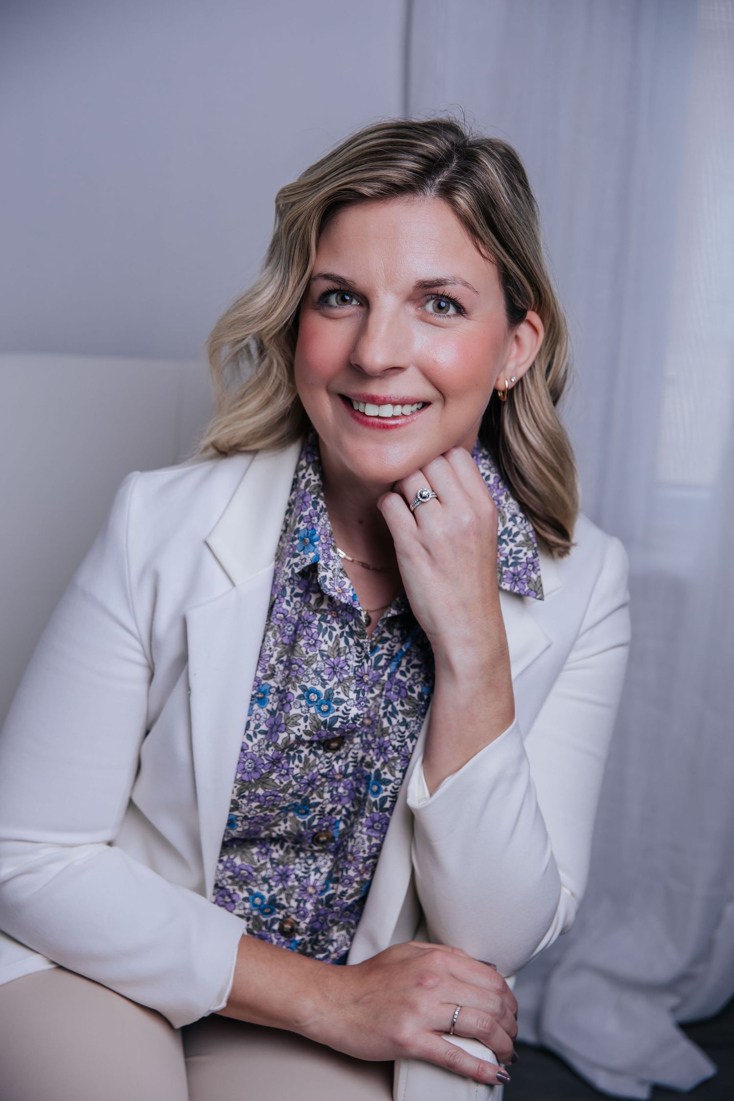 Corporate headshot of person in white blazer with sparkly blouse against light background.
