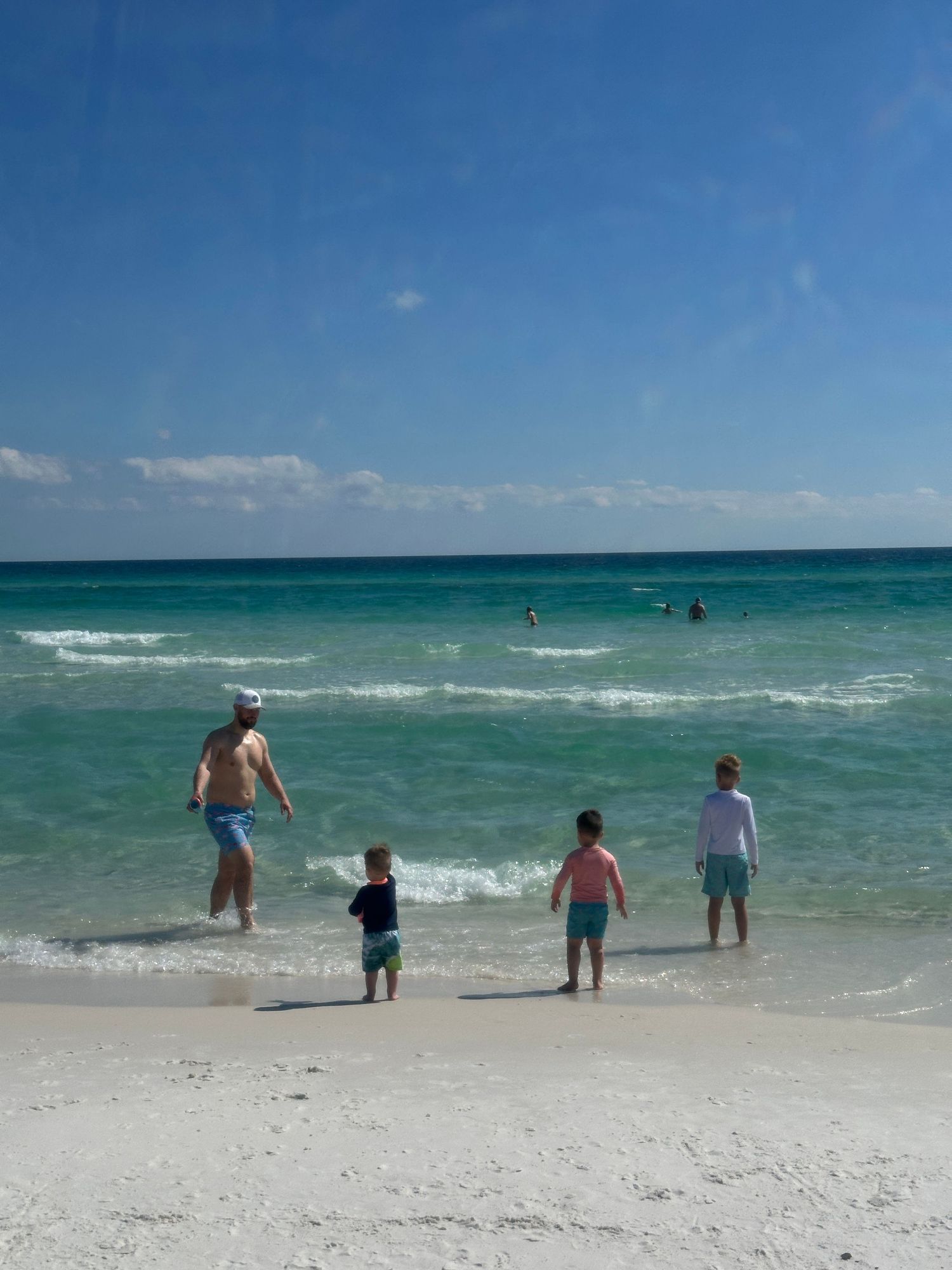 Family wading in shallow turquoise waters at a beautiful white sand beach.