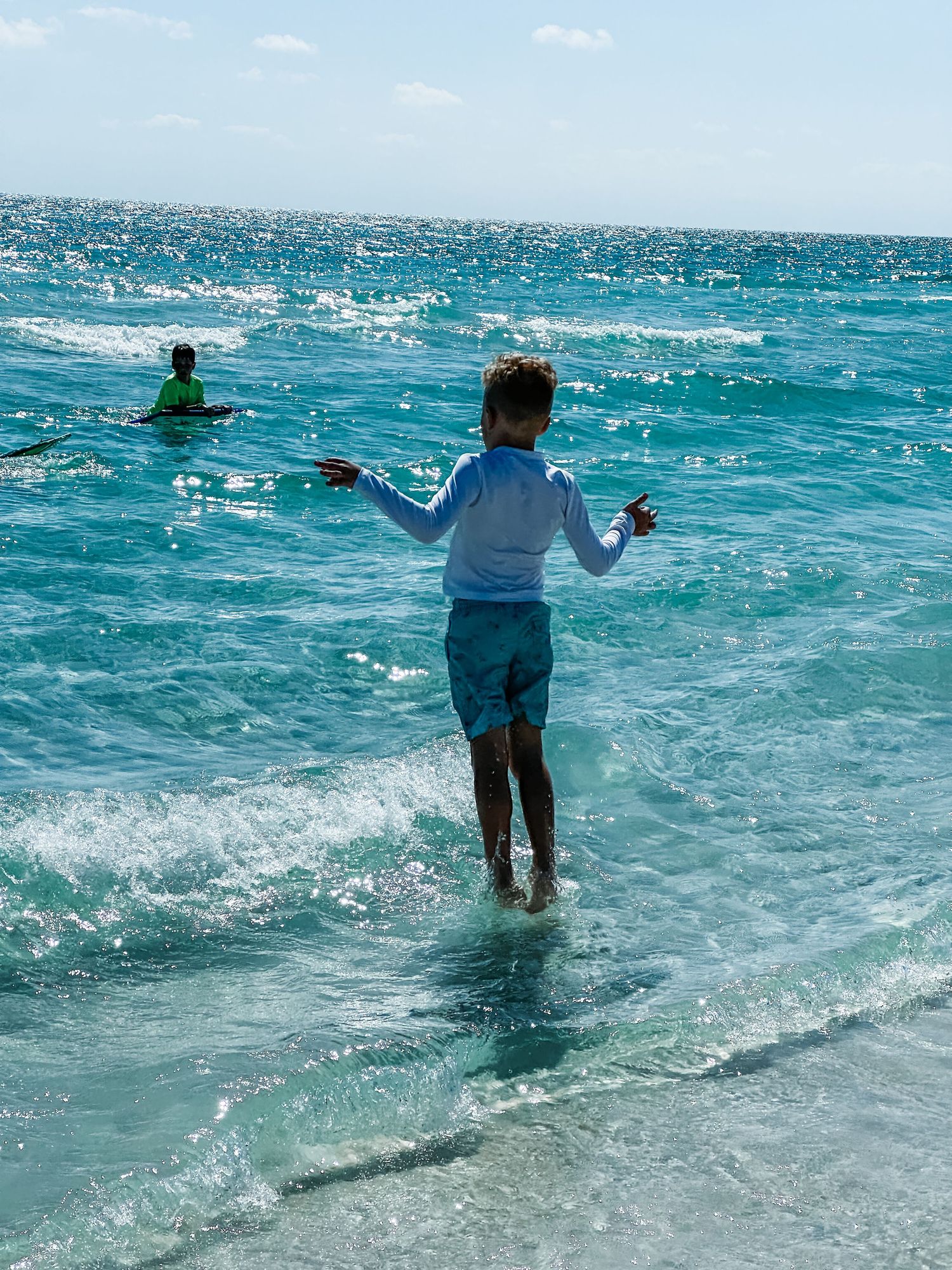 Child jumping in crystal clear turquoise ocean waves on a sunny beach day.