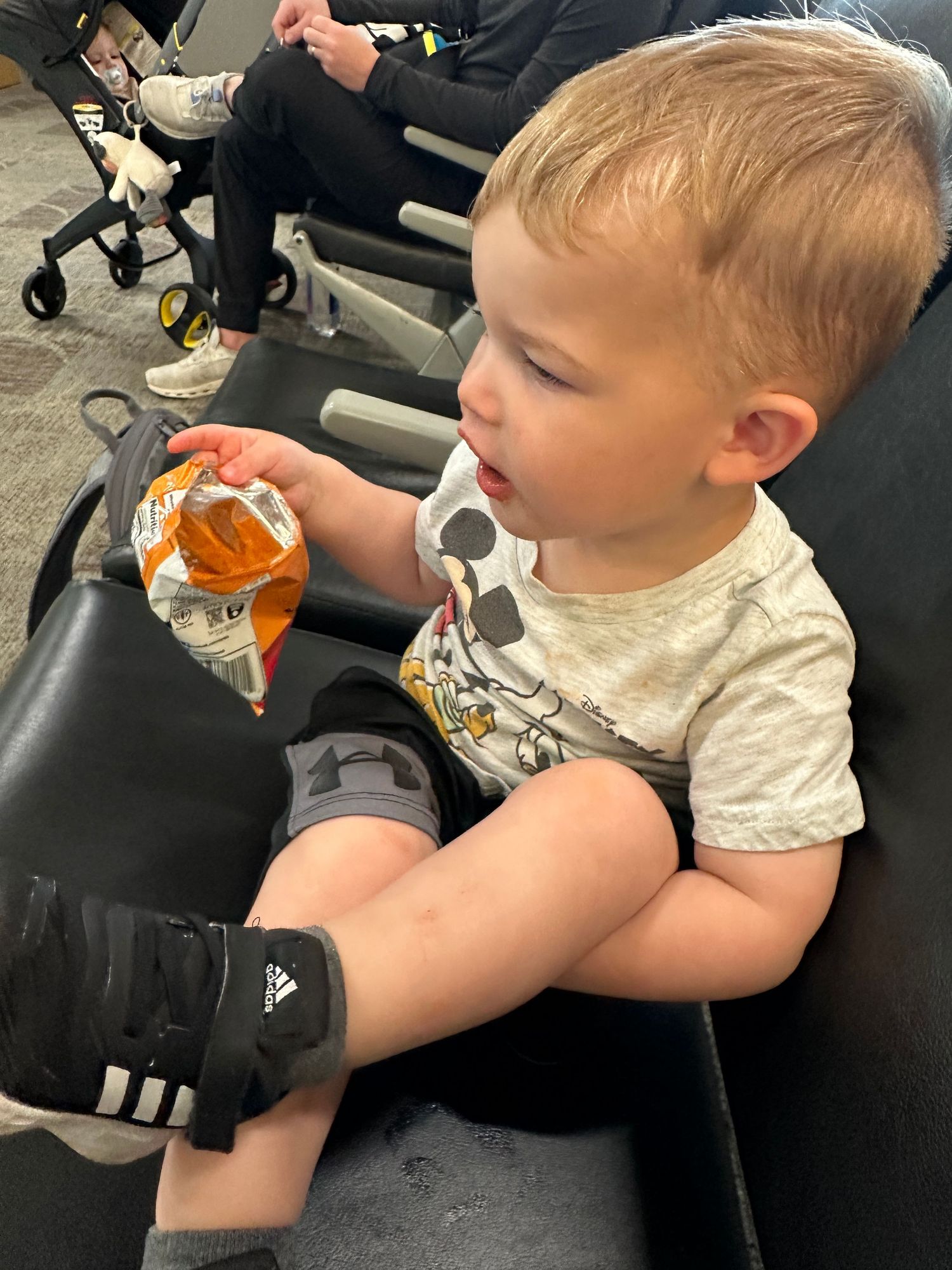Young child sitting in salon chair holding orange drink while getting haircut.