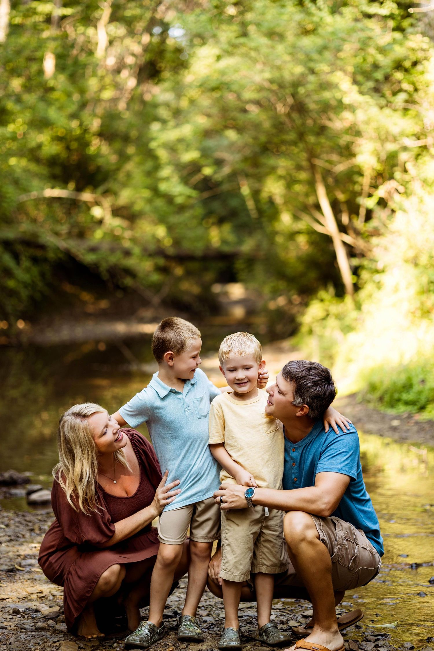 A happy family plays together by a stream on a sunny afternoon in a wooded area.