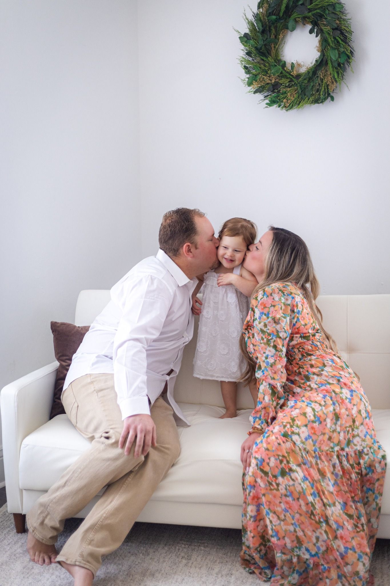 Family sharing sweet moment on white couch beneath decorative holiday wreath.