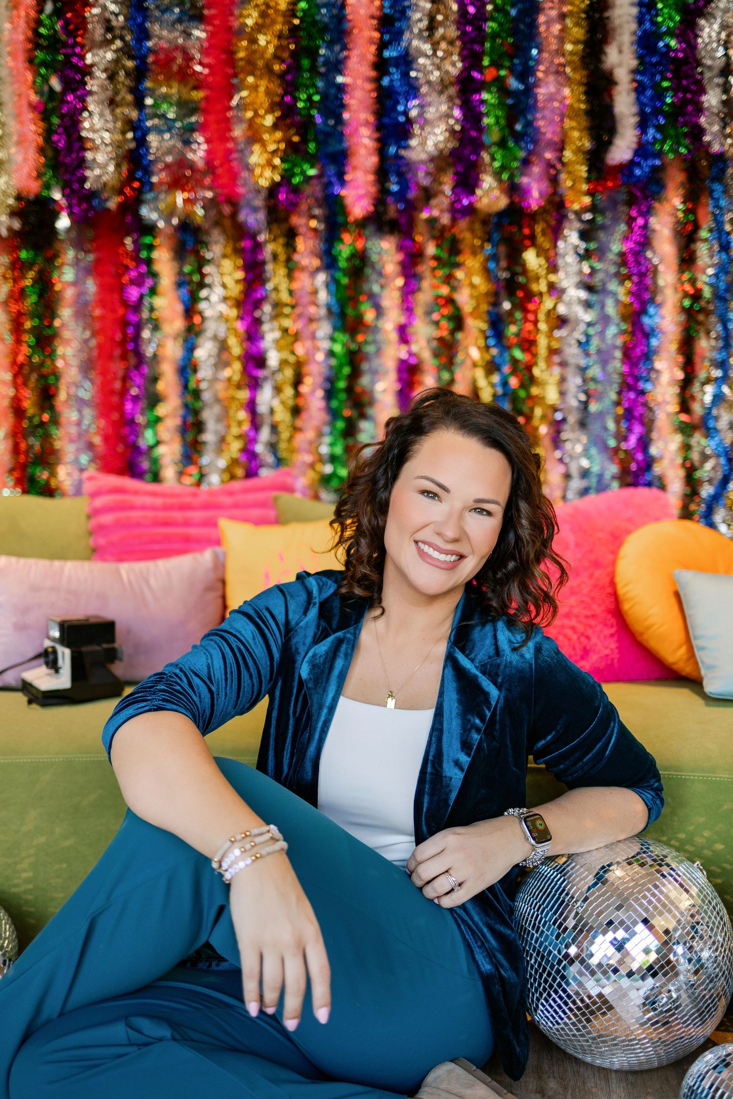 Person in blue velvet suit relaxes on green couch with disco ball and colorful tinsel backdrop.