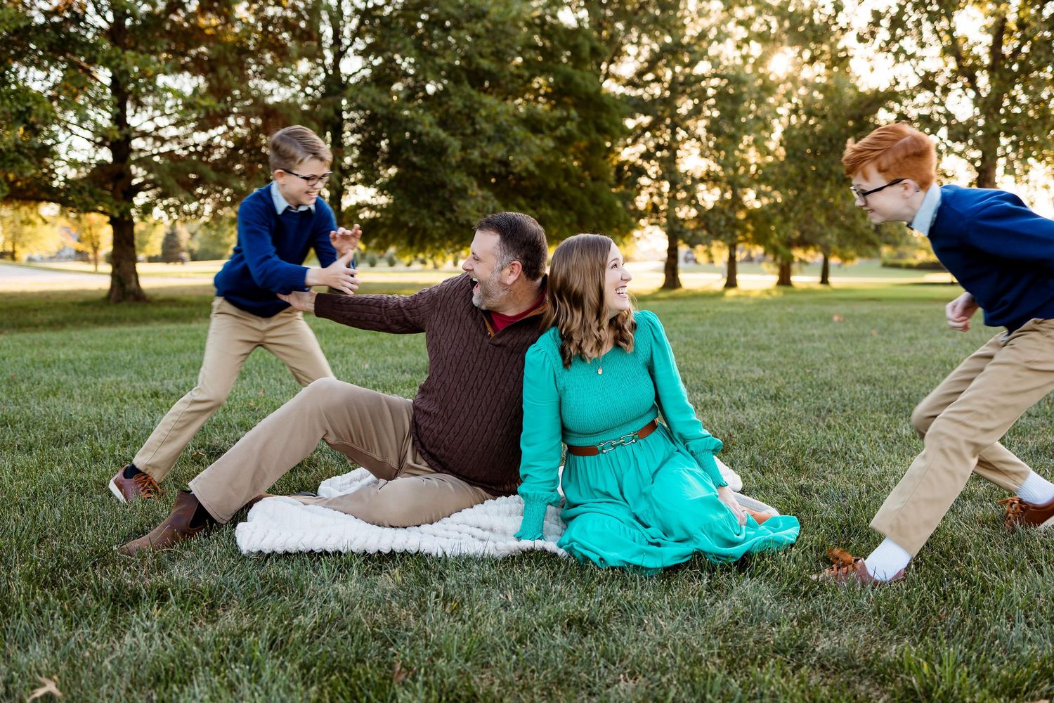 Two people in casual attire relax and laugh together while lying on green grass during a sunny afternoon.