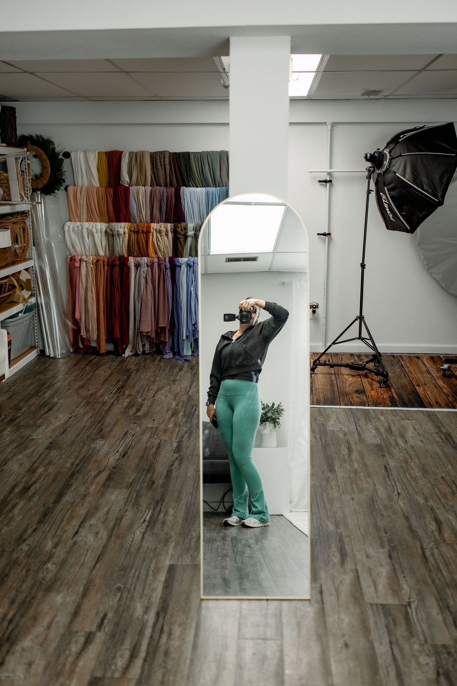 Professional photo studio space with wood floors, backdrop stands, and clothing racks along the wall.