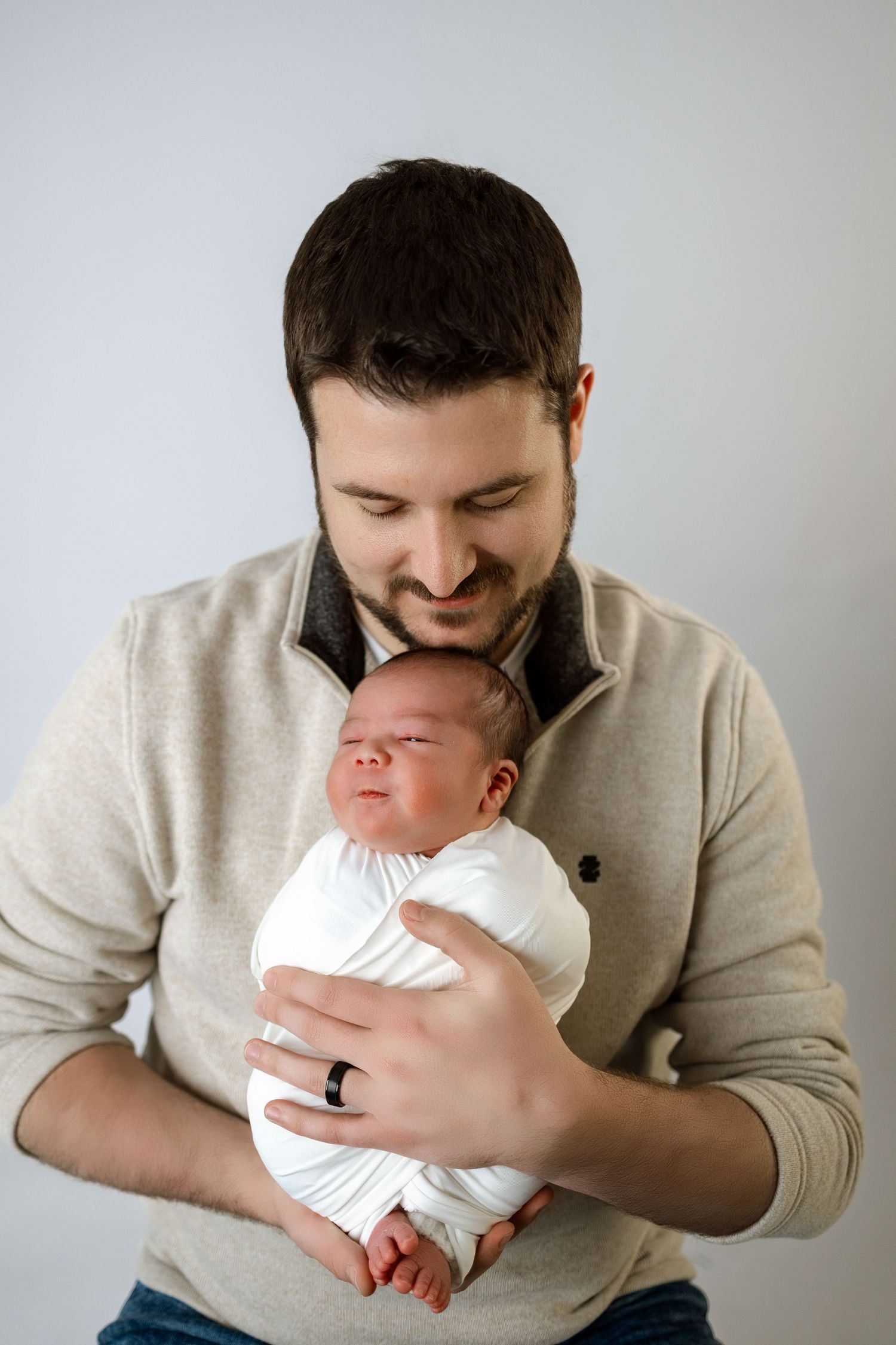 A tender moment between a parent in a beige sweater cradling and kissing a newborn baby in white clothing.