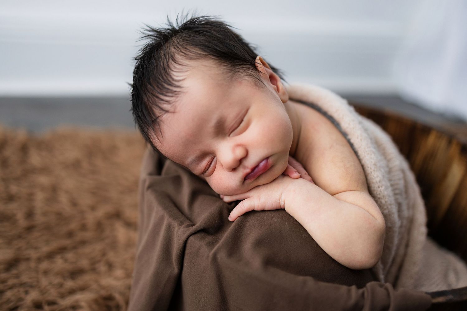 Peaceful sleeping newborn baby wrapped in brown blanket during professional photography session.