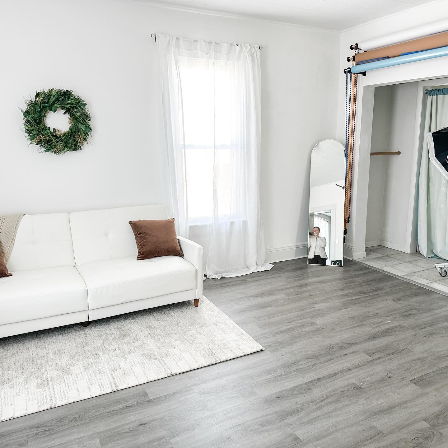 Minimalist room with white couch, wreath decor and grey flooring.