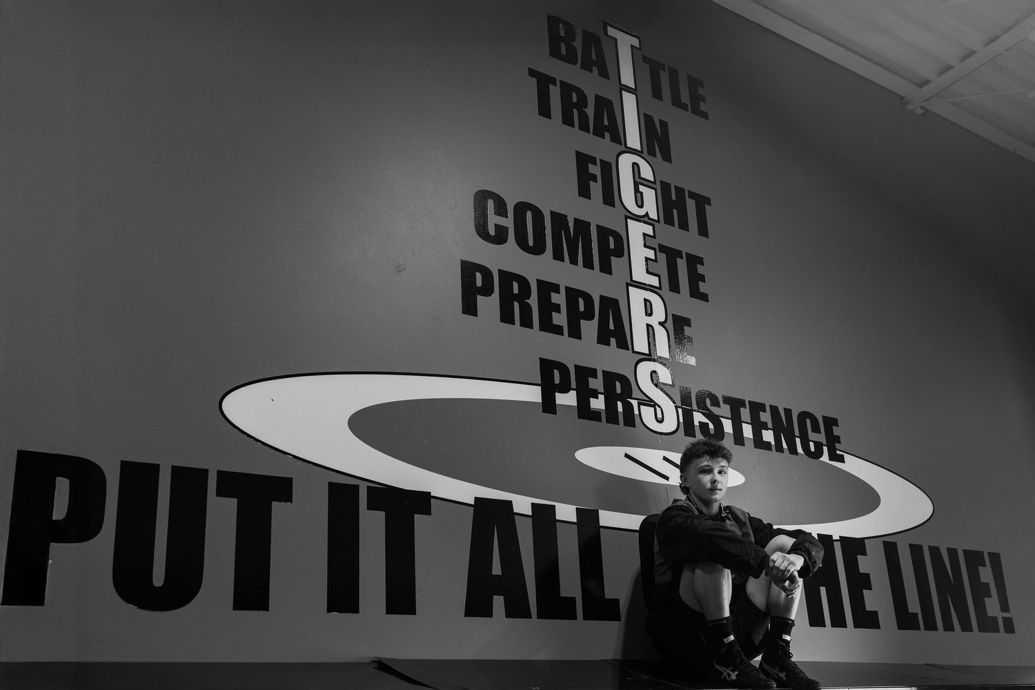 A black and white motivational sign with text displayed on a wall in an industrial or gym setting.
