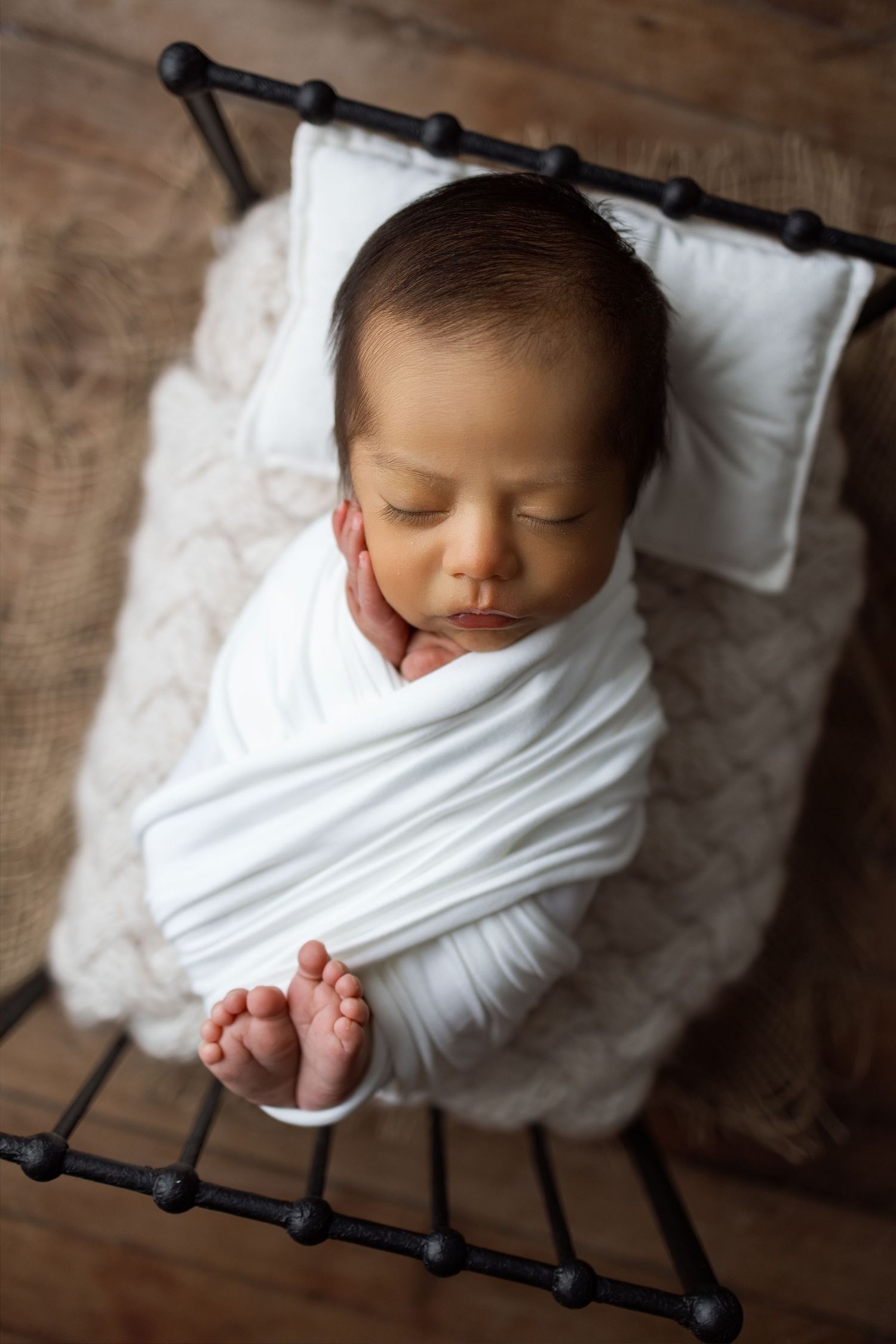 A newborn baby wrapped in white swaddling cloth lies on a rustic wooden surface in a series of artistic photos.