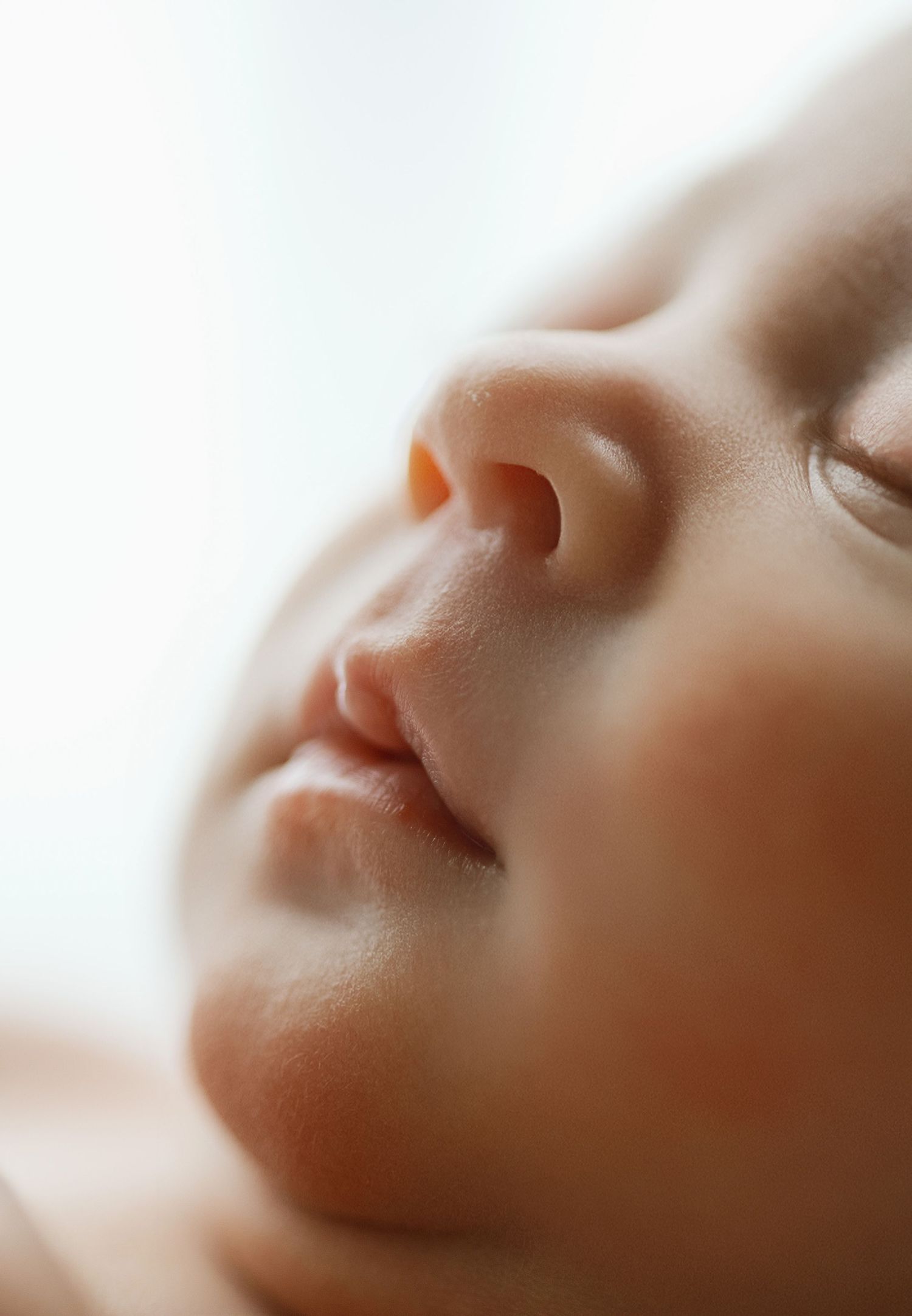 Close-up of a sleeping newborn baby's face showing delicate features, soft skin, tiny nose and lips.