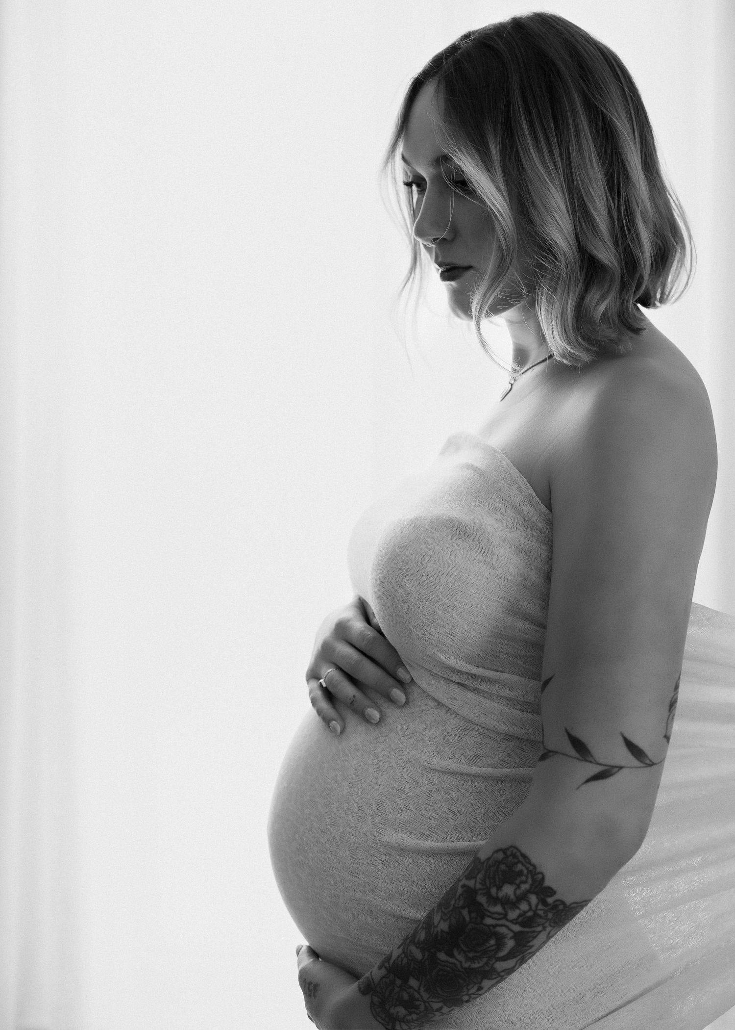 Black and white maternity photo series showing pregnant woman in white fabric against light background.