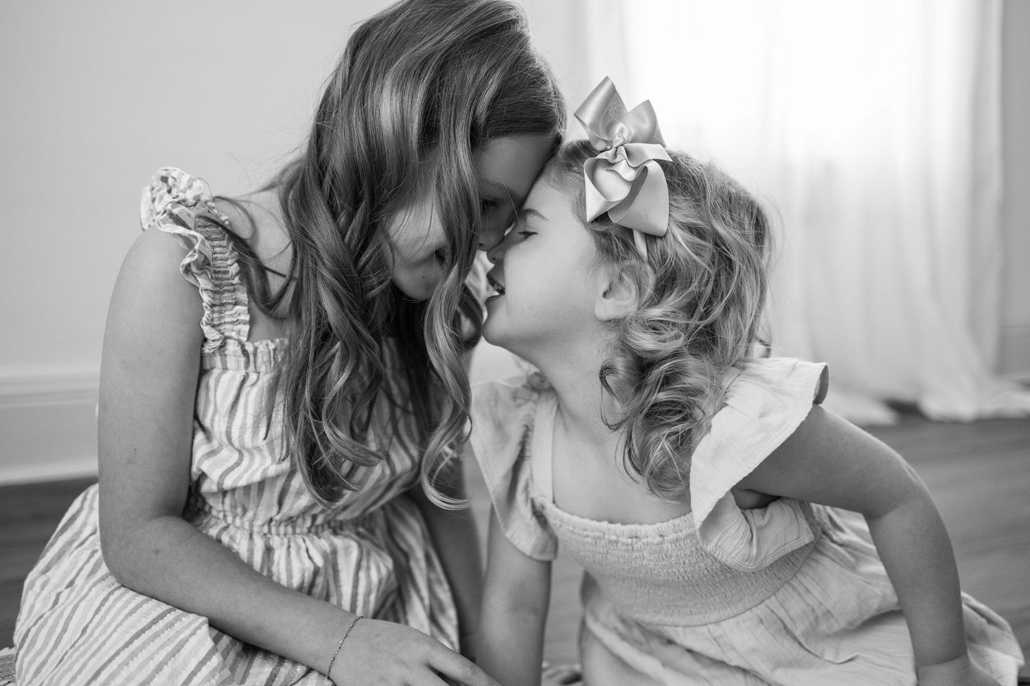A tender black and white portrait of mother and daughter in ruffled dresses sharing an intimate moment together.