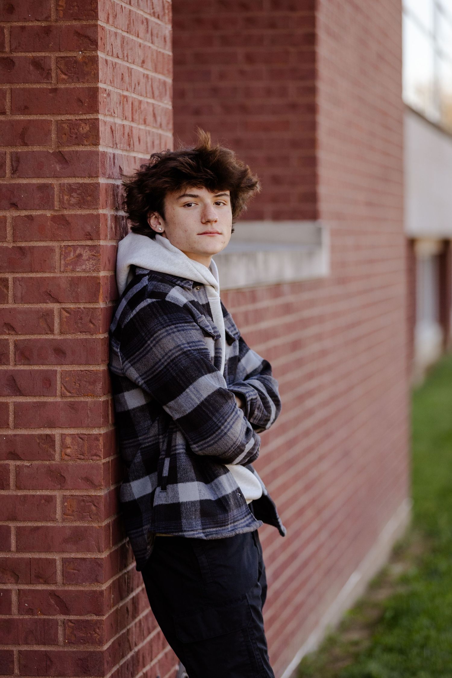 Portrait against brick wall wearing plaid flannel jacket and white hoodie.