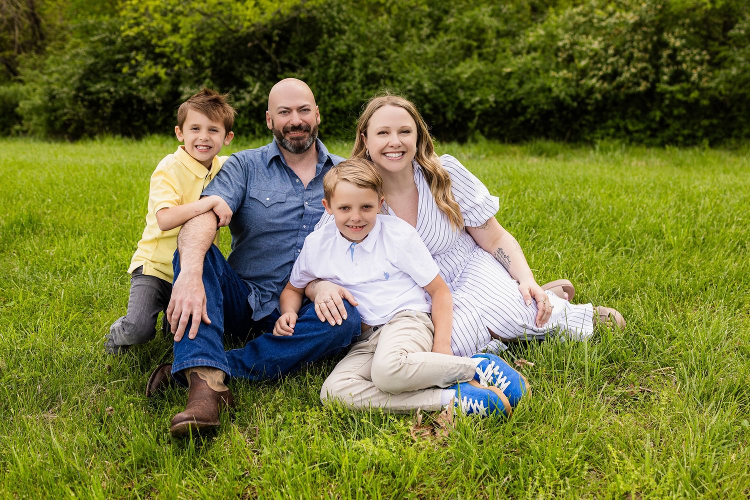 Family of four sitting together on green grass for outdoor portrait.
