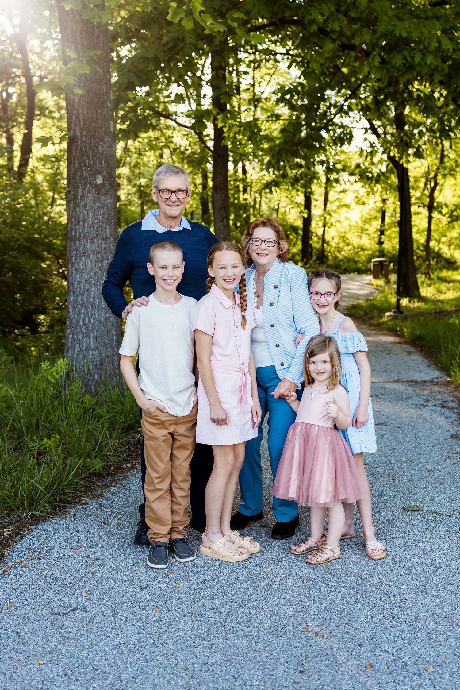 Group portrait of family members on a gravel path surrounded by lush green trees.