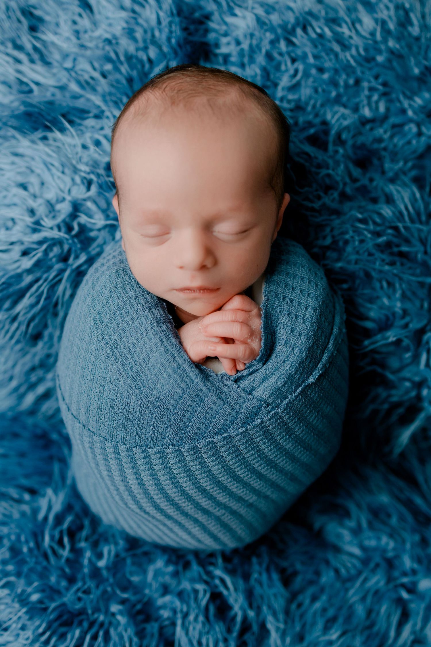 Sleeping newborn wrapped in soft blue blanket on matching blue furry background in multiple artistic angles.