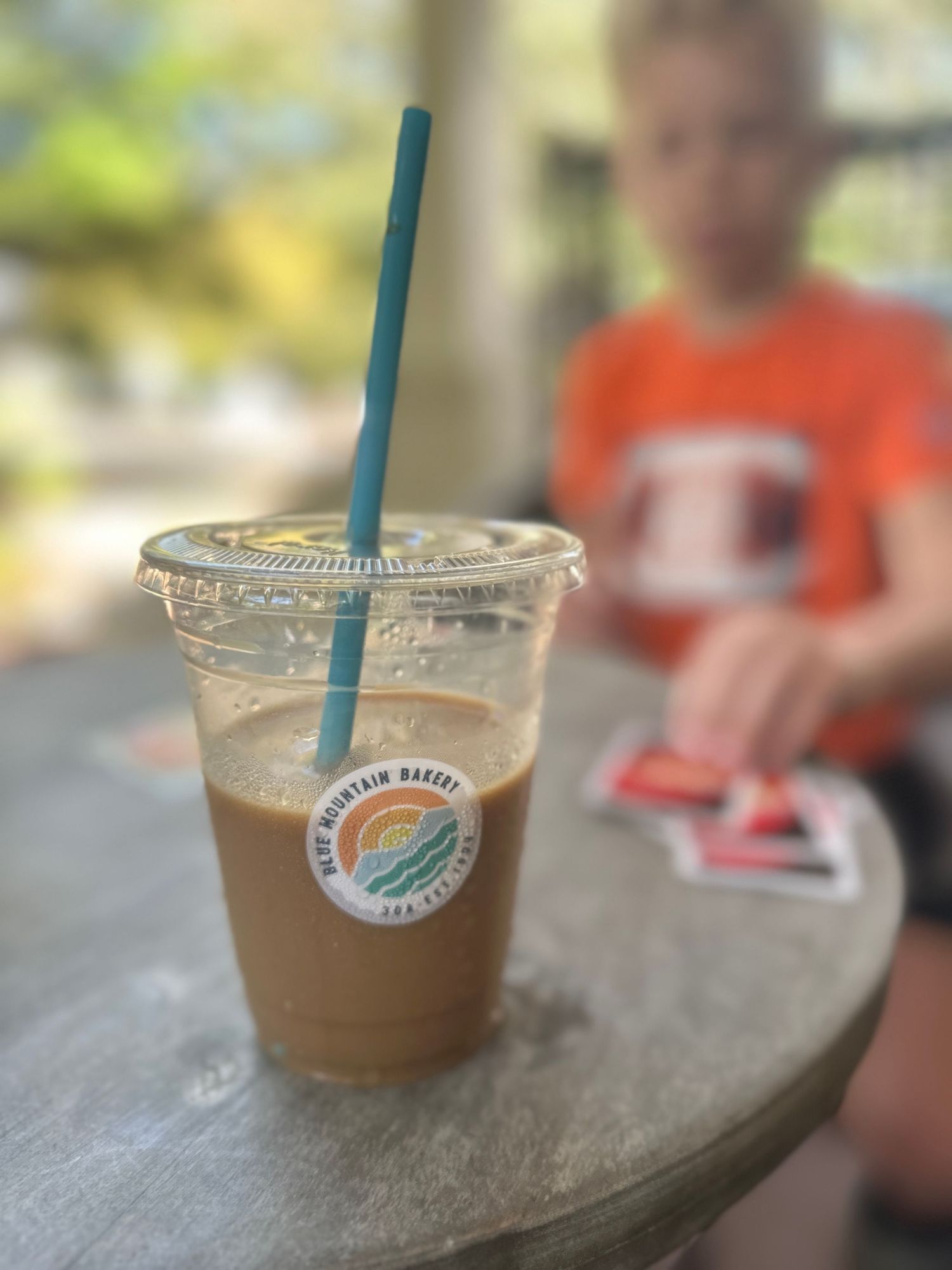 Iced coffee drink with blue straw on wooden table at cafe.