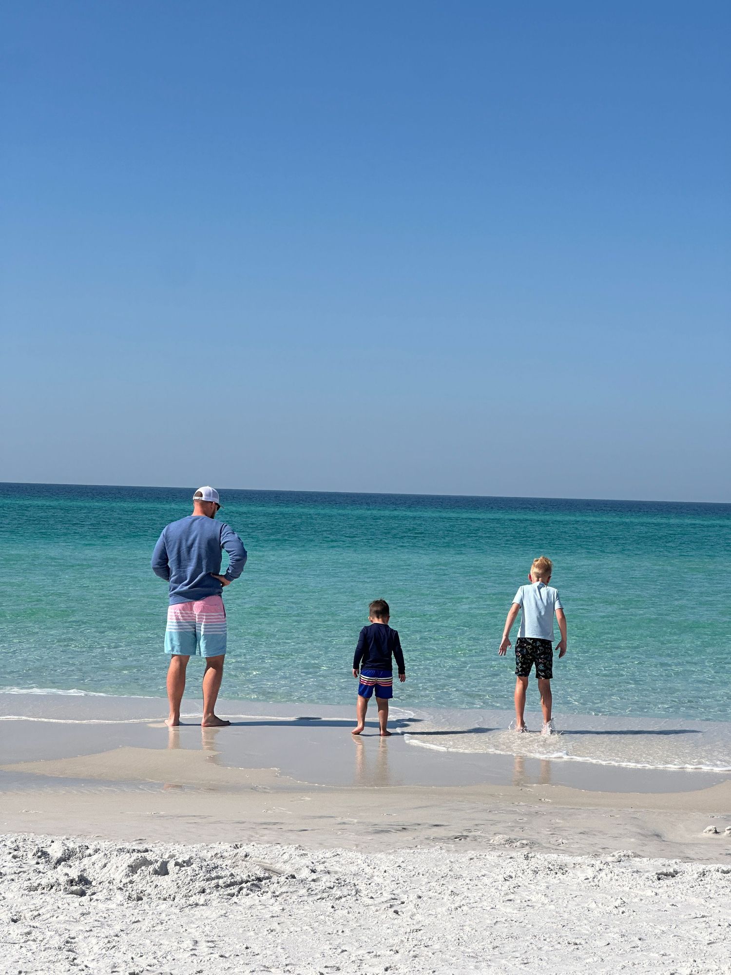 Three beachgoers stand at the water's edge enjoying the turquoise ocean view on a sunny day.