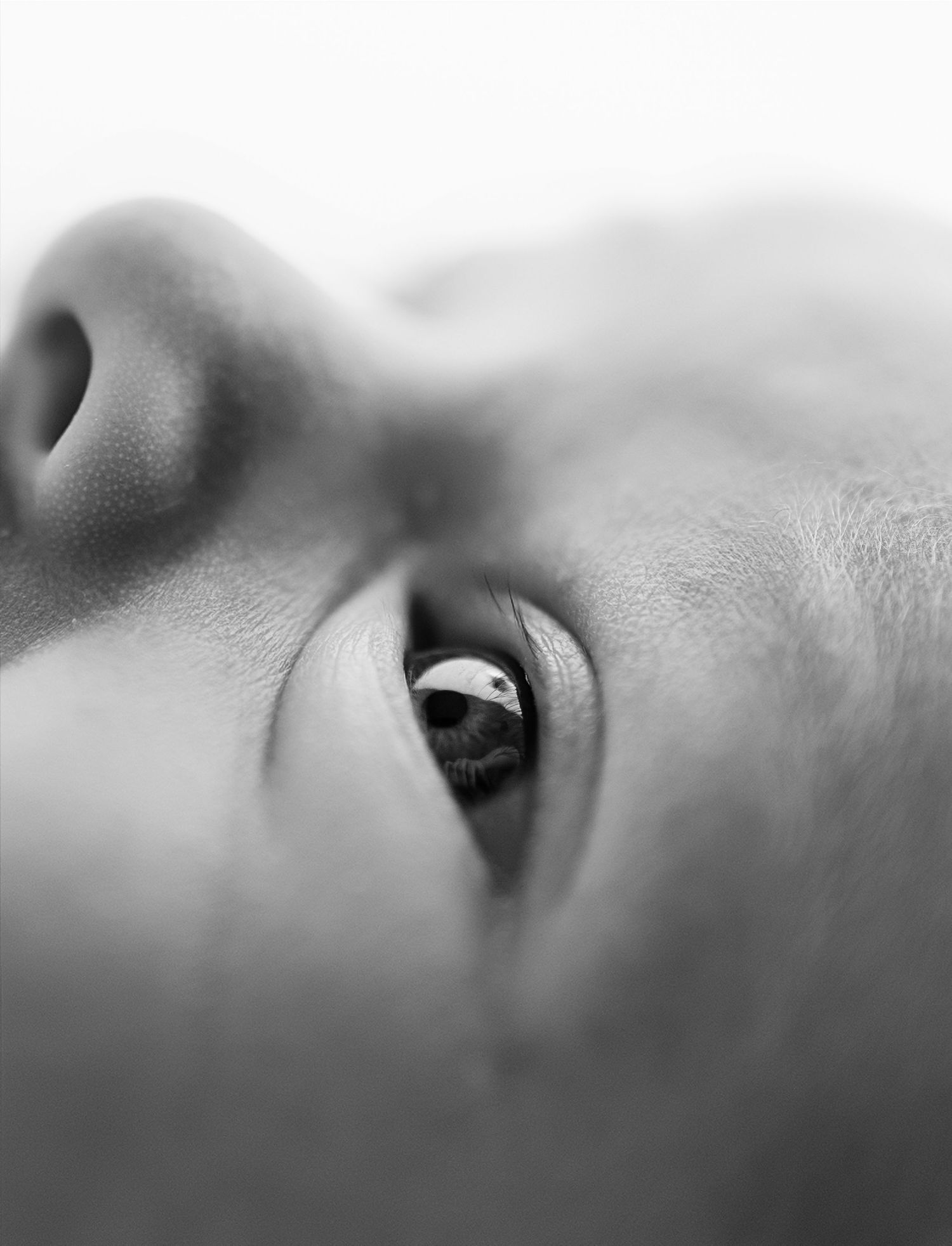 Close-up black and white macro photo of a baby's eye and nose, capturing delicate skin texture.