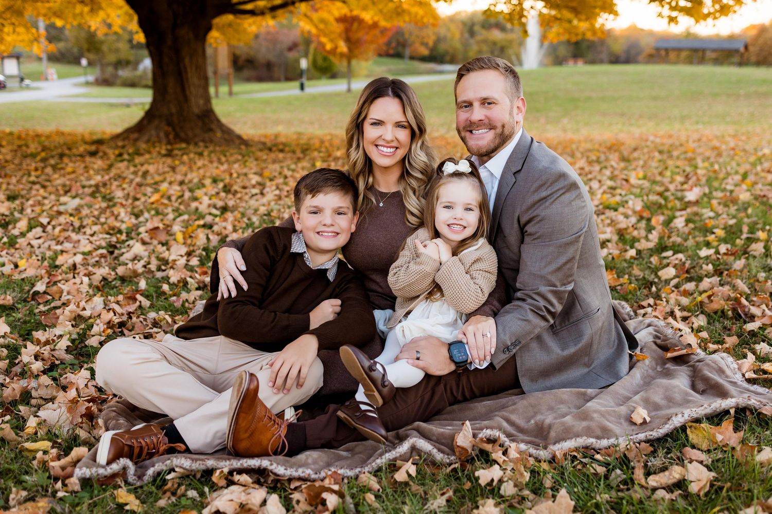 A family sits together on a blanket surrounded by vibrant autumn leaves during a fall photoshoot in a park.