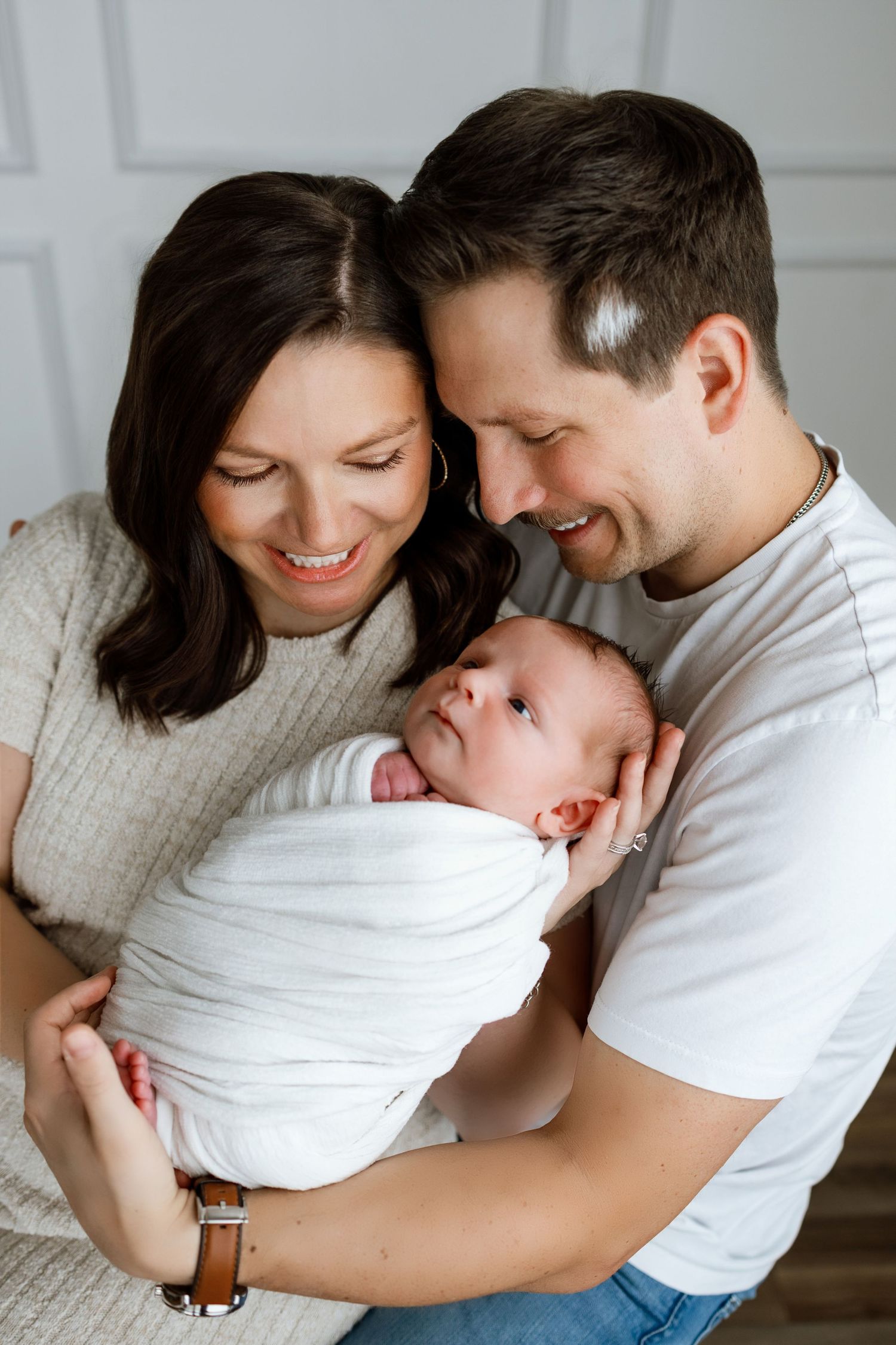 Parents smiling while holding their swaddled newborn during a newborn photography session in Edwardsville, Illinois