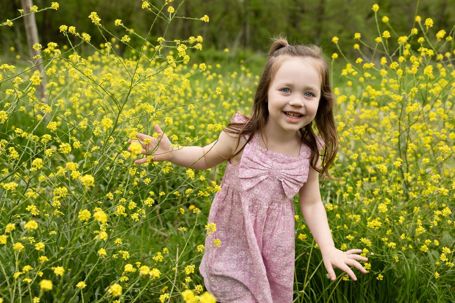 Young girl in pink dress playing joyfully among yellow wildflowers.